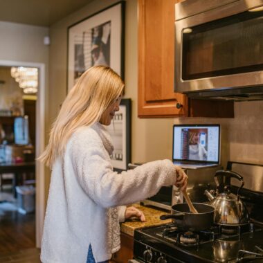 A woman cooks while attending an online class from her laptop in the cozy kitchen.